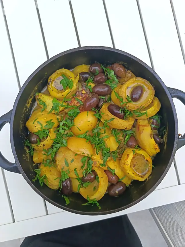 Fruits jaunes, olives et herbes fraîches dans une cocotte noire, vus du dessus