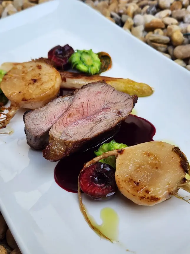 Bœuf rosé, pommes de terre et jus sombre sur une assiette rectangulaire blanche