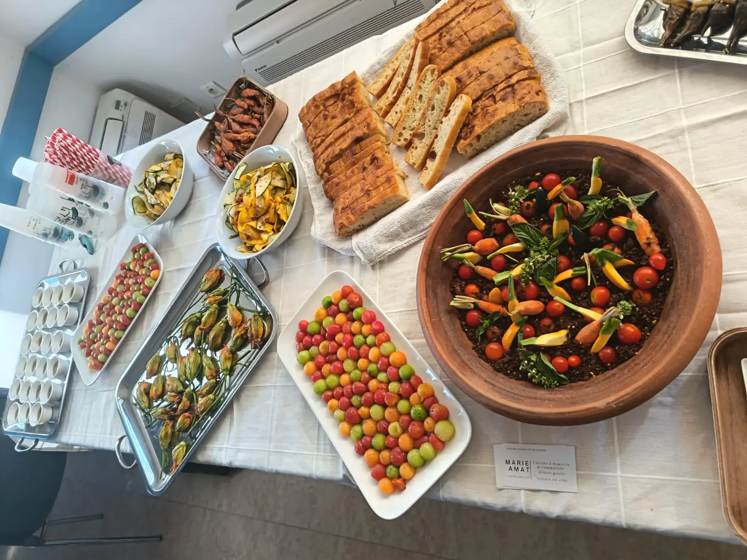 Grande table de buffet : bol en terre cuite de tomates et de petites carottes, plaques de plats et tomates multicolores